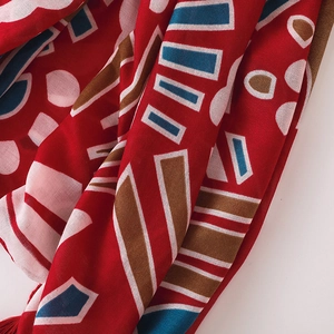Gros plan sur l'écharpe en coton-lin rouge avec motifs géométriques et pompons