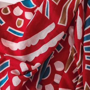 Détail macro d'une écharpe ethnique rouge avec motifs géométriques sur tissage léger