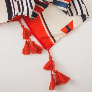 Détail d'une écharpe bohème aux rayures géométriques et pompons en coton orange