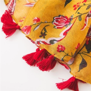 Detail of bohemian yellow floral scarf featuring vibrant red tassels and fine cotton texture