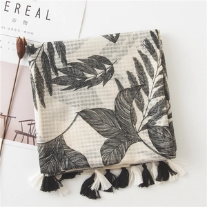 Flat lay of linen scarf with leaf prints, fringe detail, and artistic props