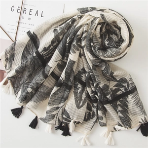 Cotton linen shawl with black tropical leaf print and tassel fringe on white background