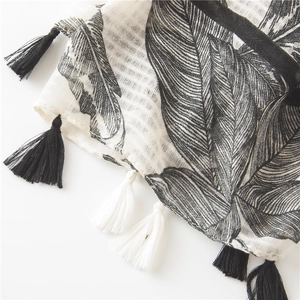 Detail of cotton linen scarf showing tropical leaf print and black and white fringe tassels