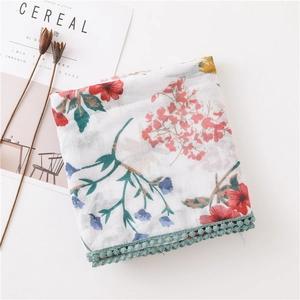 Détail d'une écharpe à fleurs avec bordure à pompons turquoise et coton doux