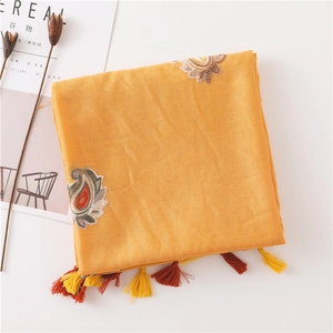 Detail of yellow cotton linen scarf featuring paisley embroidery and tassel trim on white