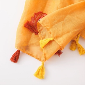 Close-up of lightweight orange linen shawl with embroidery and colorful tassels