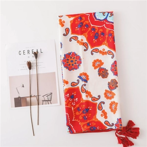 Boho-Sonnenblumen-Strandtuch mit roten Quasten, präsentiert auf einem weißen Schreibtisch