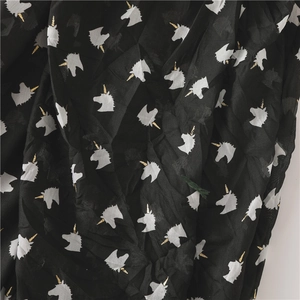 Detail of thin black beach shawl with white unicorn patterns and gold print details