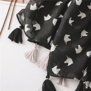 Detail of black beach scarf with white unicorn prints and tassels with gold metal beads