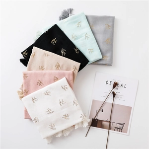 Detail of light cotton-linen scarves featuring golden swallow prints and tassel edges