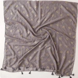 Detail of dark grey scarf with golden swallow patterns and fringe trim on white background