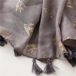 Macro shot of grey linen scarf featuring gold foil swallow patterns and fringe details