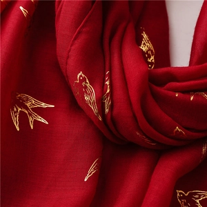 Detailed macro view of golden swallow foil prints on elegant crimson red cotton linen scarf