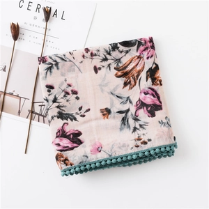 Détail d'une écharpe fleurie en coton et lin avec motifs colorés et pompons bleu canard