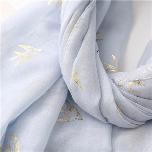 Macro detail of light blue cotton-linen scarf with elegant gold foil swallow patterns