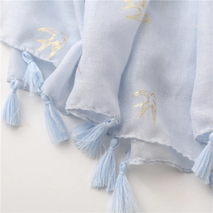 Macro shot of light blue scarf featuring elegant gold swallow prints and tassel edges