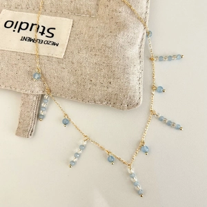 Détail macro du collier doré avec glands bleu clair et perles de cristal sur lin