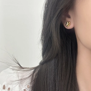 Elegant gold flower stud earrings with central crystal shown on a female model