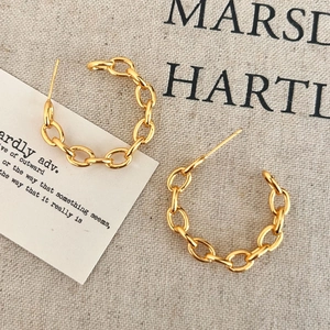 Detail of gold chain link C-shape hoop earrings on minimalist textured background