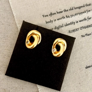Elegant gold twisted oval stud earrings with clear zircon on a black display card