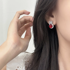 Elegant silver bow stud earrings with red gemstones and zircons on model's ear