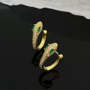 Détail macro de boucles d'oreilles serpent dorées avec zircons et yeux en pierre verte