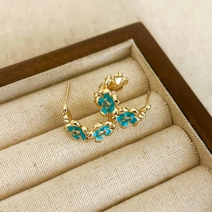 Dettaglio macro di orecchini a fiore dorati con smalto blu e pavé di zirconi brillanti