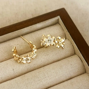 Dettaglio di orecchini floreali dorati con smalto bianco e zircone brillante
