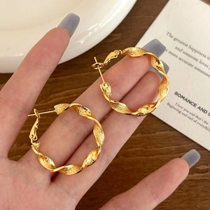 Macro detail of luxury golden twisted hoop earrings with textured finish on hand
