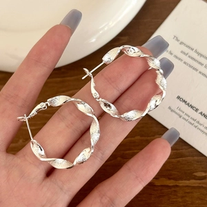 Detailed close-up of silver twisted hoop earrings with frosted texture and luxury finish