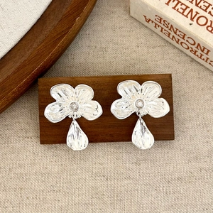 Detail of silver floral earrings with zircon center and teardrop pendant on wooden stand