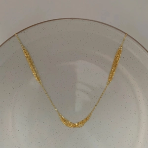 Detail einer minimalistischen mehrlagigen vergoldeten Kette auf einer grauen Keramikplatte
