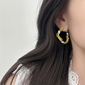 Close-up of twisted silver hoop earring with bright yellow crystal beads on ear
