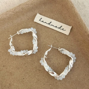 Close-up of twisted crystal hoop earrings with silver metal base on a handmade tag