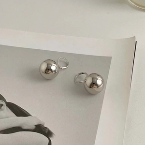 Macro detail of high-polish silver metal ball earrings on a minimalist art magazine