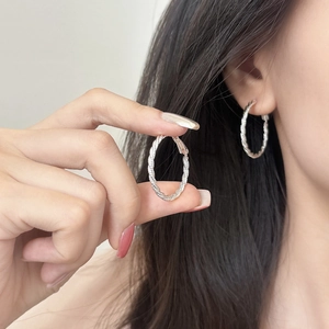 Fashionable silver twisted hoop earrings featuring a polished spiral texture on model