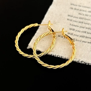 Macro detail of golden twisted rope texture on large metallic hoop earrings