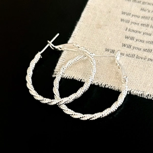 Detail of silver twisted hoop earrings with woven texture on a textured fabric
