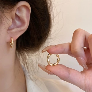 Minimalist gold twisted rope hoop earrings shown on ear and held by hand for scale
