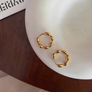 Macro detail of gold hoop earrings with woven texture on a white ceramic plate
