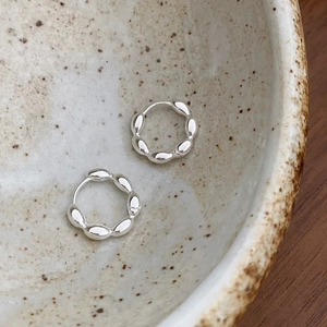 Close-up of silver hoop earrings with olive-shaped bead texture on a vintage ceramic bowl