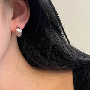 Silver shell-shaped huggie earrings with textured ribbed design worn on earlobes