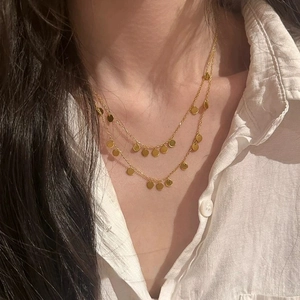 Chic layered gold necklace with polished round disc pendants worn on neck with white shirt