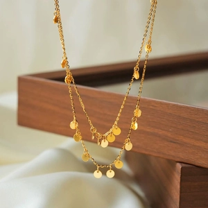 Detail of layered gold-tone necklace featuring circular sequins on a white silk backdrop