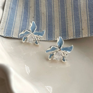 Vue macro des boucles d'oreilles orchidée bleue et zircon sur une assiette blanche