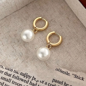 Elegant gold drop earrings with white shell pearls on a rustic linen background