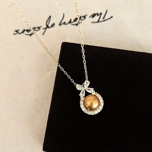 Macro shot of gold pearl necklace with zircon bow pendant on black velvet display