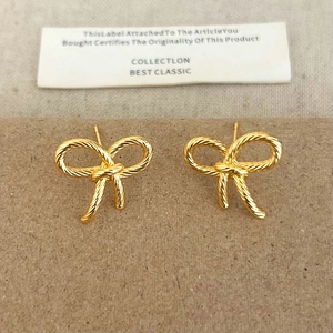 Detailed close-up of golden bow-shaped stud earrings with vintage woven rope texture