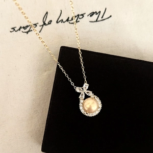 Detail of gold bow necklace with champagne pearl and zircon pendant on jewelry box