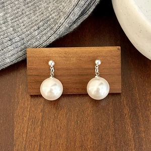 Détail de boucles d'oreilles élégantes avec perles blanches sur support en bois épuré
